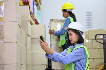 Young Asian women workers in warehouse using mobile phone to scan the QR code of product for...