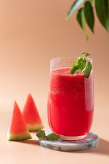 fresh watermelon drink with mint in a glass on a beige background with green leaves. clean eating and diet concept. vertical image. copy space