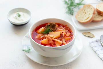 red borscht soup in a white bowl, served with sour cream, herbs and bread. Traditional Russian Ukrainian beet soup. close-up. White background.