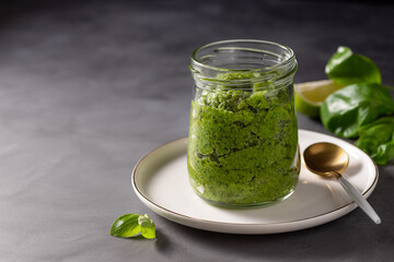 homemade green pesto sauce with basil and pine nuts in a glass jar on a dark background. Traditional Italian pesto recipe for making pasta, spaghetti, bruschetta, pizza. copy space