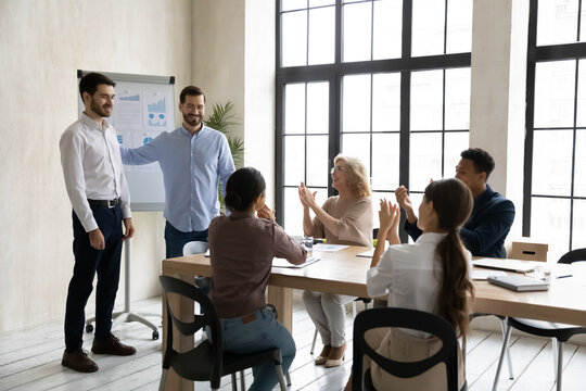 Happy different generations mixed race colleagues clapping hands, congratulating smiling male coworker with personal achievement, professional success, job promotion or birthday at meeting in office.