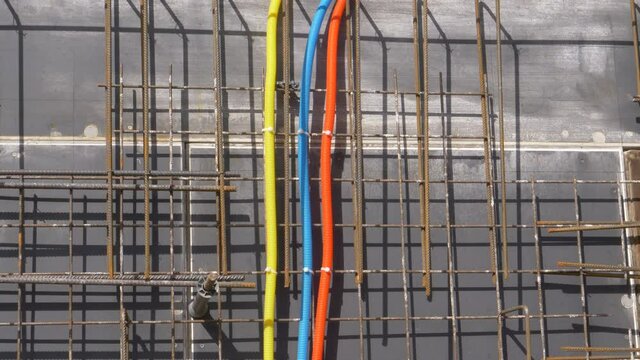 CLOSE UP: Three corrugated plastic conduits converge into single socket set installed on outer side of unfinished wall. Electricity and internet installation tubing runs along house under construction