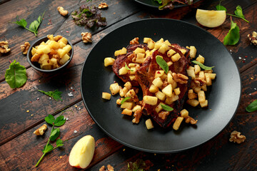 Roasted Pork chops with caramelized apples, walnuts and sage in black plate on wooden table