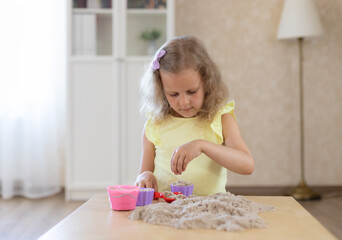 cute little girl playing with kinetic sand and sand molds in the living room. children's games indoors.