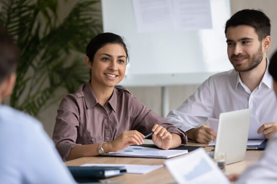 Focus on smiling young indian female manager listening to colleagues at group brainstorming meeting indoors. Millennial diverse business people discussing partnership cooperation together in office.