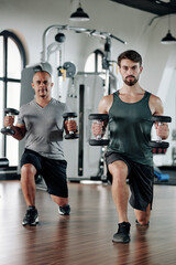 Fototapeta na wymiar Mature mixed-race man and his fitness trainer doinglunges with heavy dumbbells in hands
