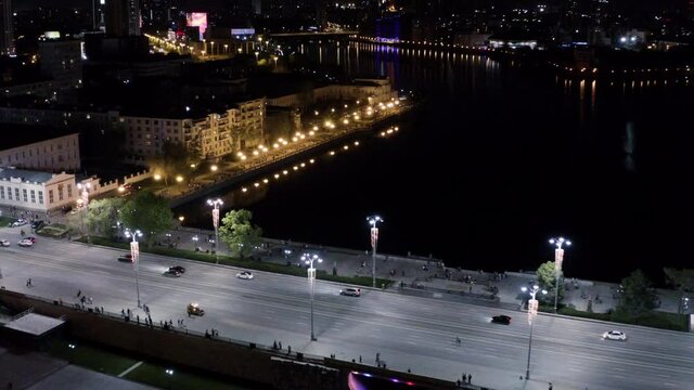 Top view of city dam with water at night. Stock footage. Beautiful view of city bridge with dark water reflecting lights at night. Night city with glowing lights reflected in water