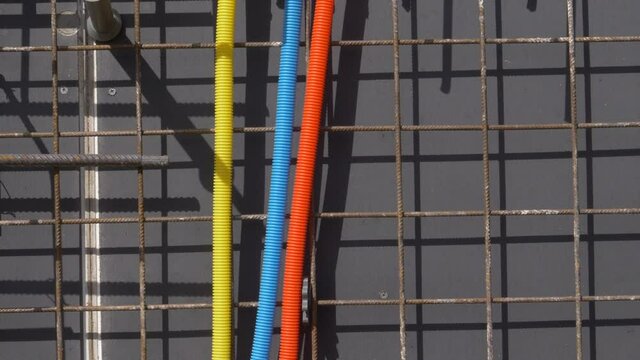 CLOSE UP: Three vibrantly colored plastic tubings lead to a socket set installed on the unfinished wall of a house under construction. Electricity and internet installation tubing runs along wall