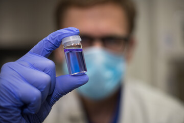 Scientist working in an analytical chemistry laboratory. Gloved hands holding a small vial of vaccine