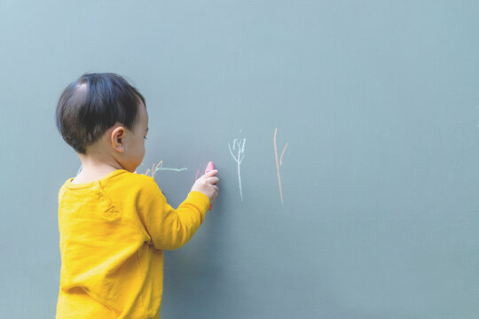 Asian little baby boy drawing with crayon chalk color on the wall, Developing concepts for learning colors and imagination.
