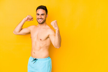 Young caucasian man with swimsuit isolated on yellow background Young caucasian man with trcheering carefree and excited. Victory concept.