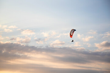 Parapente volant dans la lumière du soir sur un fond de nuages éclairés par les dernières lueurs du Soleil, Normandie, France