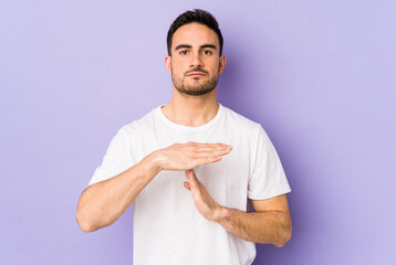 Young caucasian man isolated on purple background showing a timeout gesture.