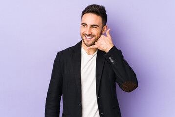 Young caucasian man isolated on purple background showing a mobile phone call gesture with fingers.