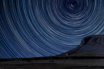Digital composite image of star trails around Polaris with landscape of Norber Ridge in Yorkshire Dales National Park - Powered by Adobe