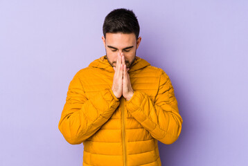 Young caucasian man isolated on purple background praying, showing devotion, religious person...