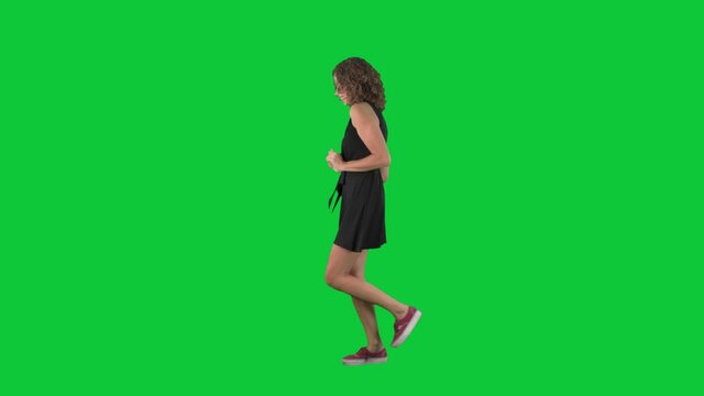 Happy woman dancing and walking listening to music. Full body side view on green screen chroma key background. 