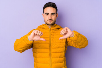 Young caucasian man isolated on purple background showing a dislike gesture, thumbs down....