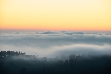 Fototapeta na wymiar Majestic landscape image of cloud inversion at sunset over Dartmoor National Park in Engand with cloud rolling through forest on horizon