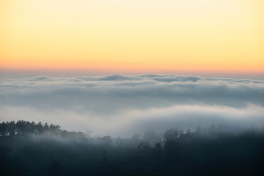 Majestic landscape image of cloud inversion at sunset over Dartmoor National Park in Engand with cloud rolling through forest on horizon