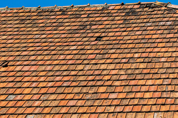 An old tiled roof with a narrow strip of blue sky. Traditional red roof with few broken parts.
