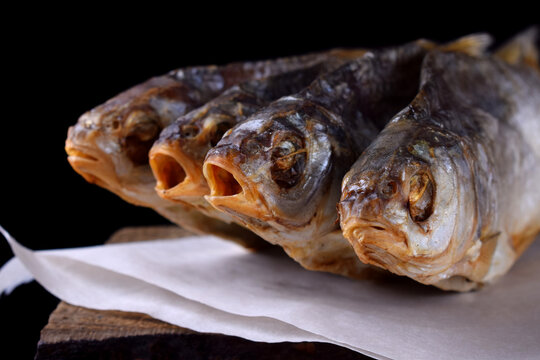Dried vobla fish on the edge of the wooden table against black background. Beer snack