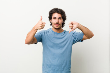 Young handsome man against a white background showing thumbs up and thumbs down, difficult choose concept