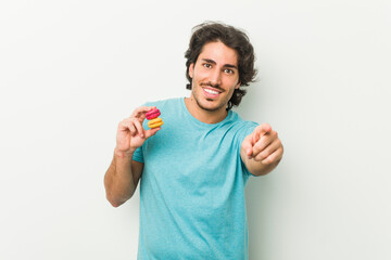 Young man holding macaroons cheerful smiles pointing to front.