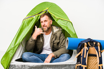 Senior inside a tent isolated on white background showing a mobile phone call gesture with fingers.