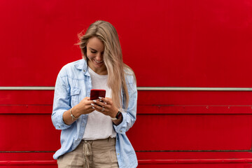 Young hipster girl using mobile phone against red background