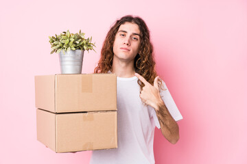 Young caucasian man holding boxes isolated pointing with finger at you as if inviting come closer.