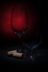 Empty glasses for wine and cognac, two corks of wine on a dark black and red background.