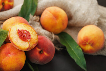 Peach fruit on a black background with a cloth of burlap and green leaves.
