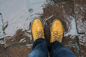 Closeup of feet of man wearing leather boots standing in a puddle of water in the street