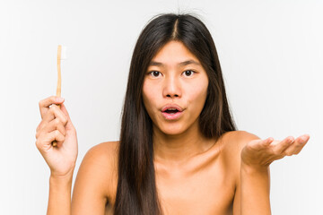 Young chinese woman holding a teeth brush isolated impressed holding copy space on palm.