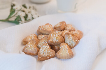 heart shaped shortbread cookies decorated with sesame seeds on a white table close-up, wildflowers and milk on the background