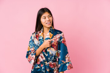 Young asian woman wearing a kimono pajamas smiling and pointing aside, showing something at blank space.