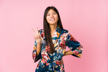 Young asian woman wearing a kimono pajamas joyful and carefree showing a peace symbol with fingers.