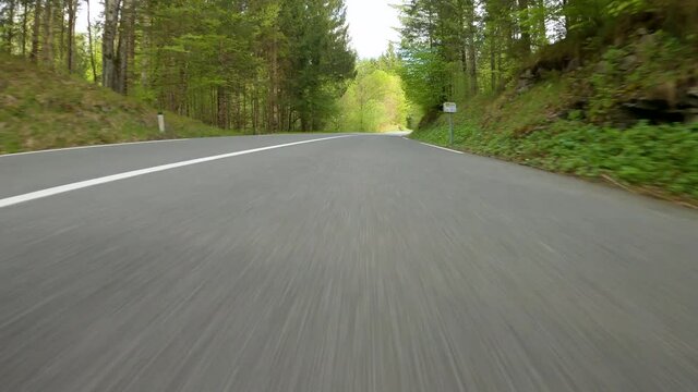 POV: Cool shot of driving along country road winding through the lush green woods. Speeding down empty winding road running through forest in a fast supercar. Sportscar joyride around the countryside.