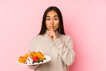 Young asian woman holding a waffle isolated keeping a secret or asking for silence.