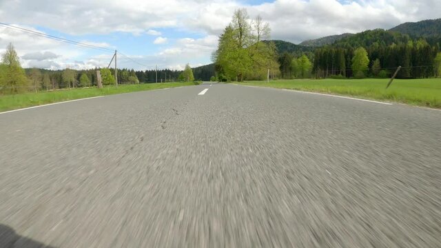 POV: Speeding down empty country road crossing a beautiful green valley on a sunny day. Racing down an empty rural road in a breathtakingly fast sports car. Picturesque scenery while driving supercar.