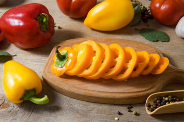 Ripe sweet yellow bell peppers are sliced. Cooking vegetable salad. Vegetables and spices on the kitchen table.