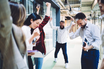 Fototapeta premium Cheerful coworkers with raised hands celebrating successful deal