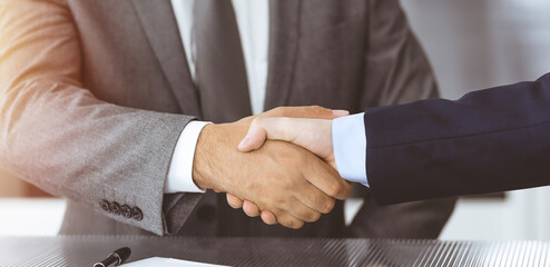 Obraz premium Unknown business people are shaking hands after contract signing in modern office, close-up. Handshake as successful negotiation ending
