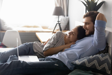 Peaceful young couple resting on cozy bed, watching romantic movie online on computer. Happy millennial family enjoying stress free weekend leisure pastime together in bedroom, relations concept.