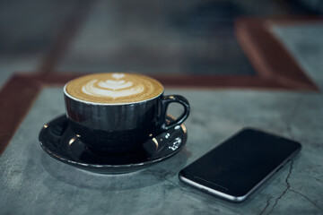 Hot cappuccino latte art and mobile phone on the table at coffee shop
