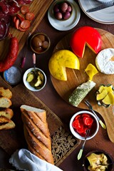 Top down view of an assortment of cheeses with bread, peppers olives and Italian sausage on wooden boards