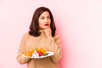 Middle age latin woman holding a waffle isolated looking sideways with doubtful and skeptical expression.