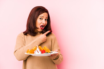 Middle age latin woman holding a waffle isolated pointing to the side