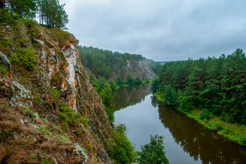 Fototapeta na wymiar Beautiful river landscape with wooded mountain slopes. Limestone rocks in the Ural mountains. Cloudy sky in the background. Natural monument 